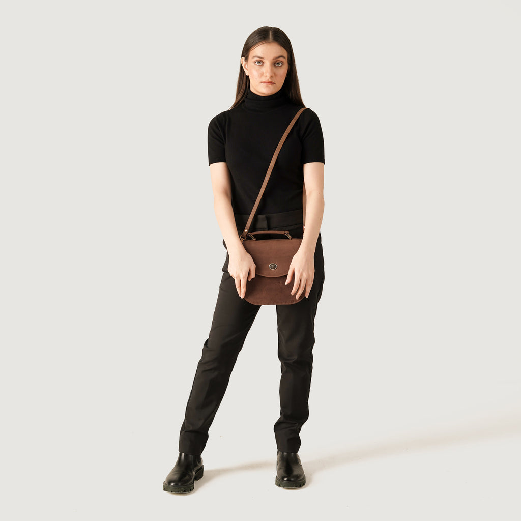 A model wearing black attire holds The Sandra Vintage Tan Leather Saddle Bag, showcasing its stylish design and versatility.